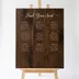 Custom wedding seating chart sign in walnut-stained birch on a pale wood easel, "Find Your Seat" engraved in script above nine numbered tables of guest names in three columns