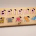 Angled view of the wood name puzzle showing the board thickness and the finger-lift holes above each letter and animal piece