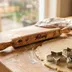 Engraved wood rolling pin resting on a floured wooden counter next to a rolled-out round of dough and cookie cutters