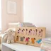 Wood name puzzle spelling Briana leaning against a stack of children's books beside a plush lamb toy on a nursery shelf