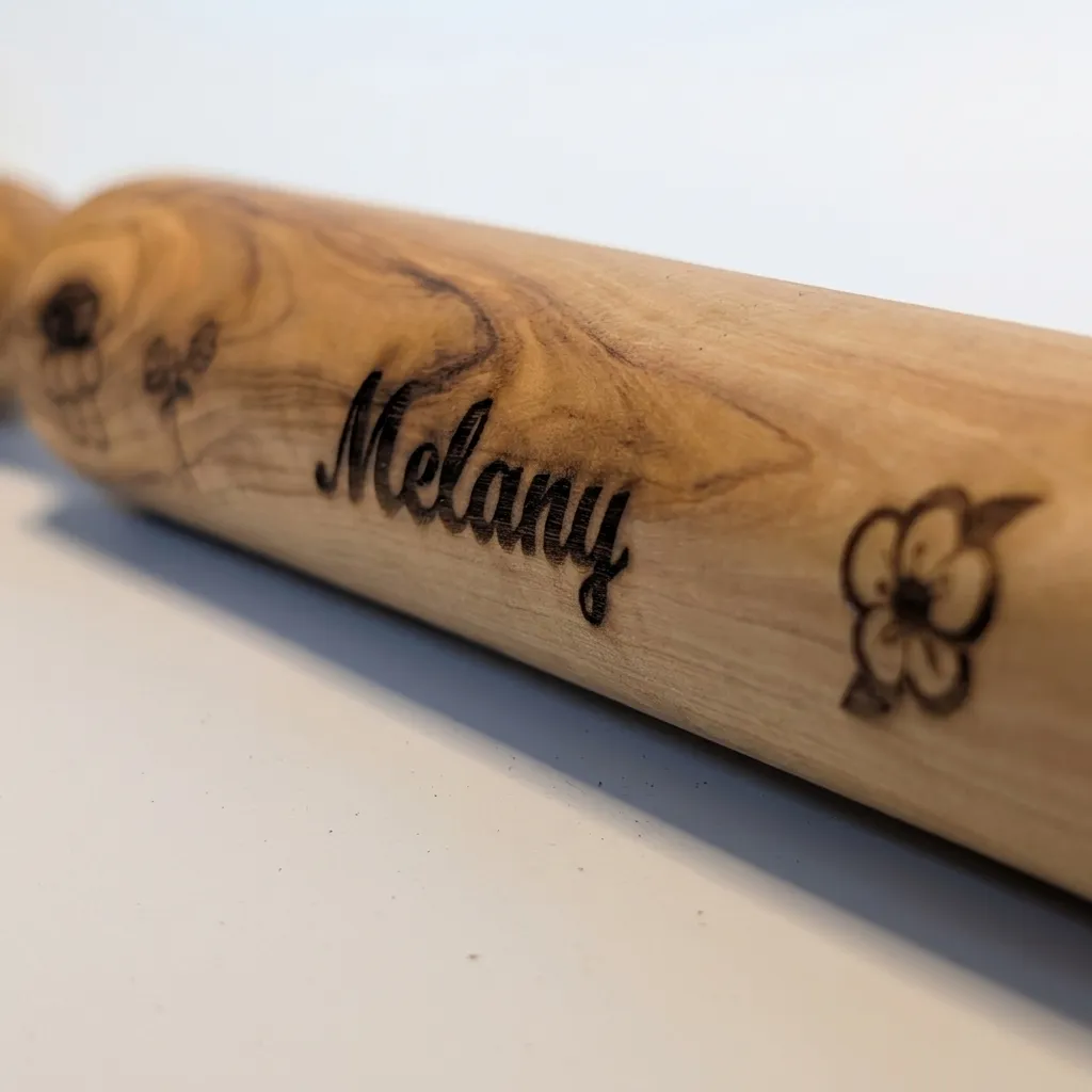 Close-up of the laser-engraved script name and flower detail on the wood barrel, showing the depth of the burn line against the grain