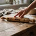 A hand reaching for the rolling pin on a flour-dusted wood counter, showing the piece at real-world scale