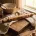 Editorial-style photo of the rolling pin on a rustic table beside a baking bowl, dried herbs, and garlic cloves