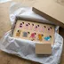 Wood name puzzle spelling Briana nestled in tissue paper inside an open kraft gift box beside a blank kraft note card