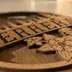 Angled macro of the walnut-stained mountain name sign showing the raised banner layer, the shadow gap beneath it, and the engraved columbine petals