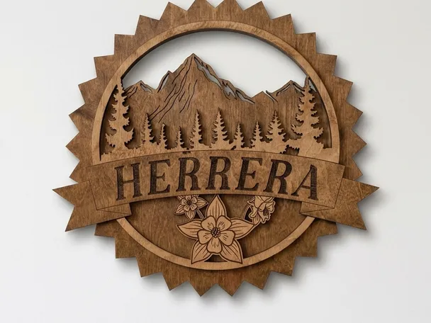 Round layered walnut-stained mountain sign on a plain light wall: a sawtooth ring, mountain range with pine trees, the name Herrera on a raised ribbon banner, and columbine flowers below