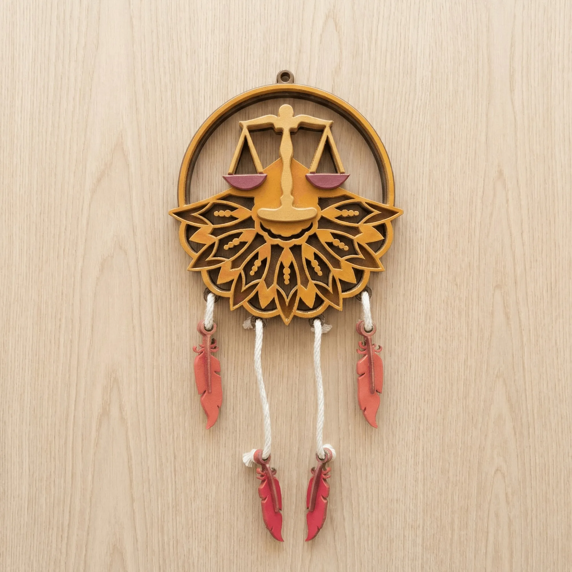 A layered wood Libra zodiac wall hanging with painted scales, petals and feather charms, hanging against a pale wood wall