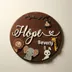Round dark walnut name sign hanging on a warm neutral wall, each raised painted piece casting its own small shadow