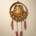Layered wood Libra zodiac wall art hanging on a warm neutral wall, the gold ring and petal mandala casting soft shadows and the feathered cords hanging free below