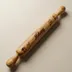 Wood rolling pin lying diagonally on a warm neutral surface, the wandering grain and dark streaks running the length of the barrel