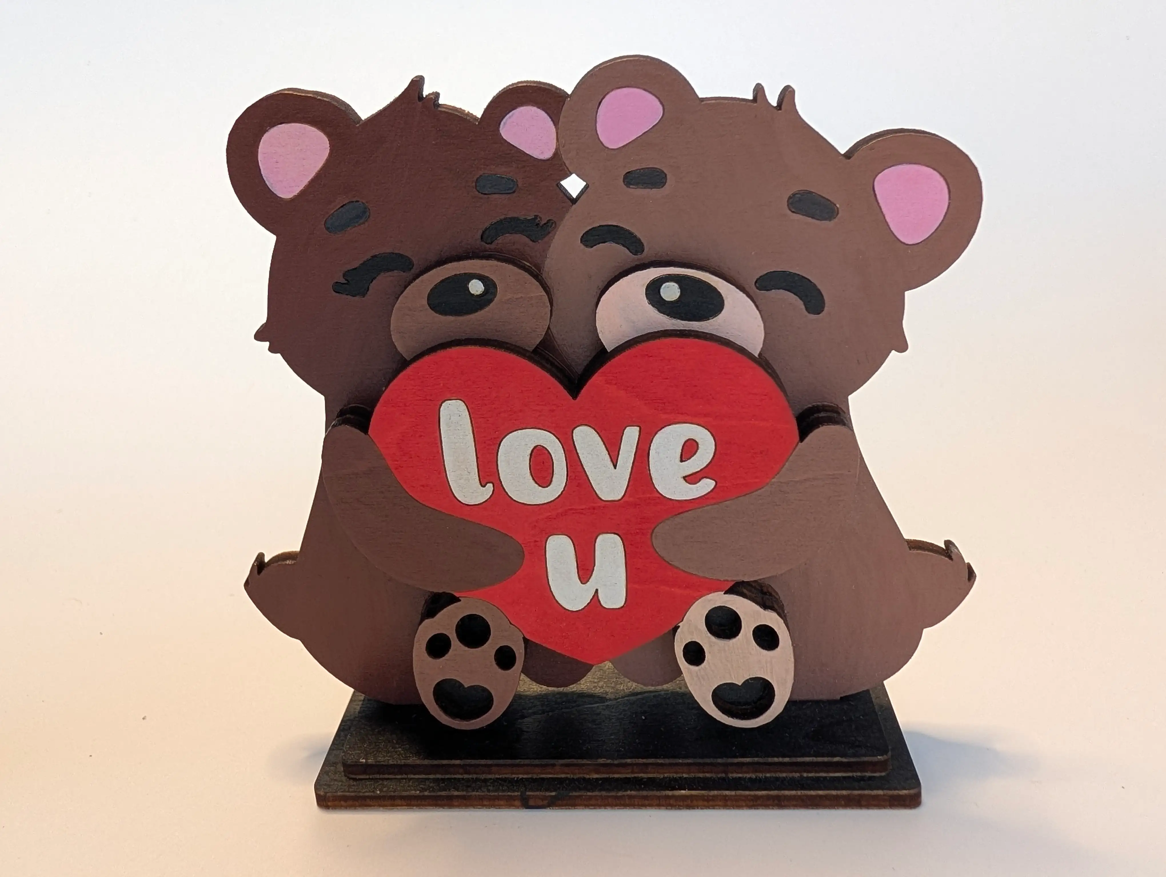 Two brown teddy bears cut from layered wood and hand-painted, hugging a shared red heart reading "love u" in white lettering, mounted on a dark-stained wood base